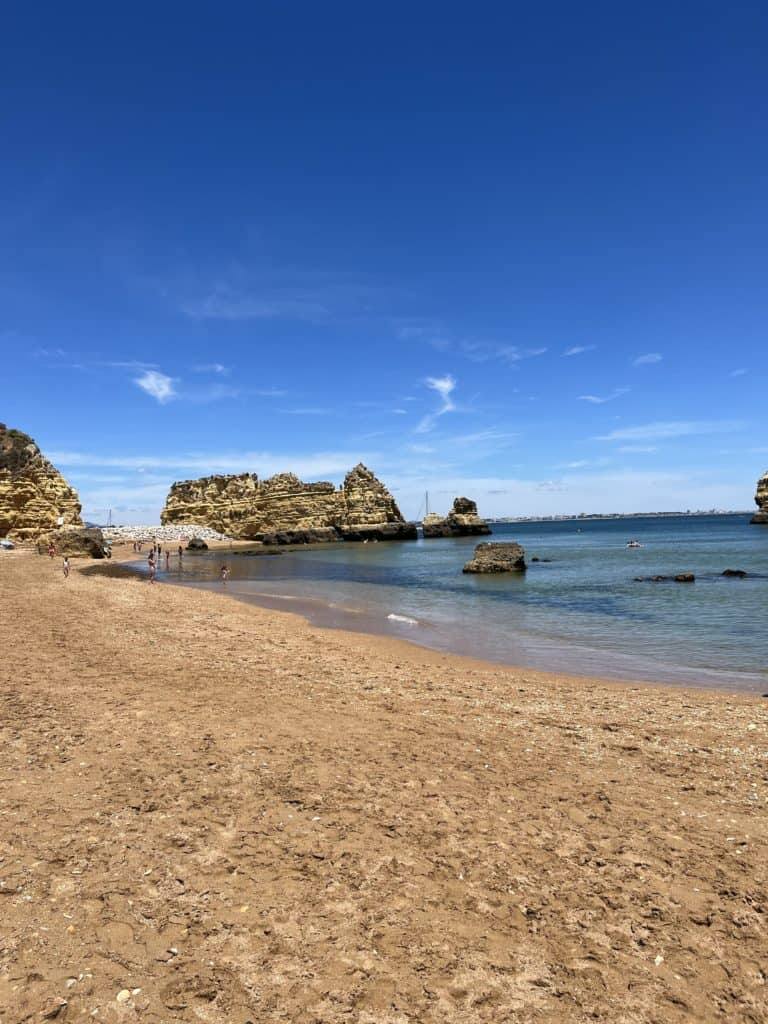 an empty sandy Praia Da Batata beach with large rock formations in the water