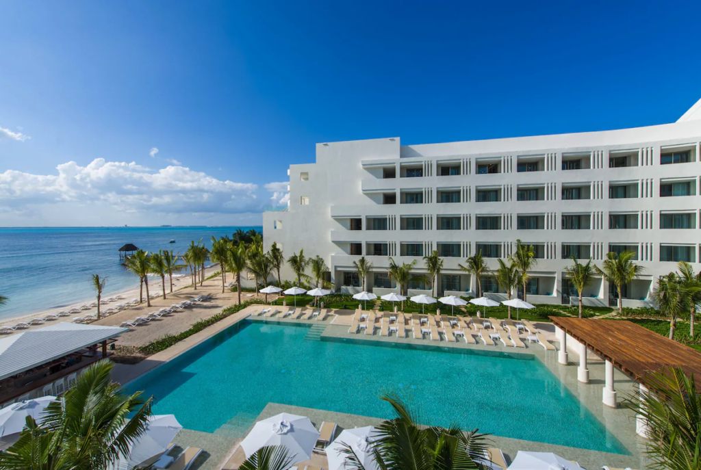 the main pool area at Izla Hotel, along with the beach steps away from the pool and several palm trees surrounding the areas