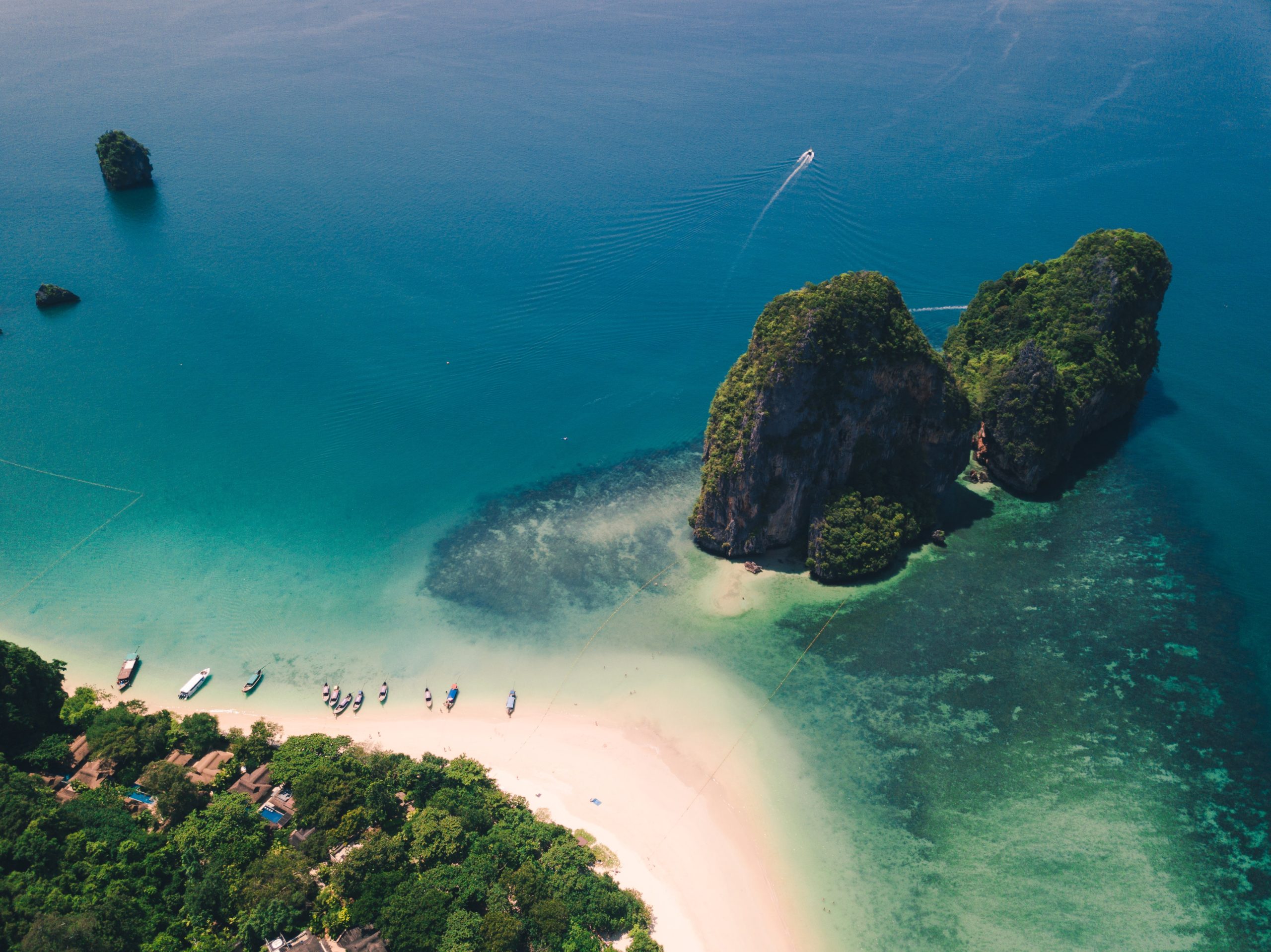 Aerial view of a stunning beach in Krabi, Thailand, featuring dramatic limestone formations rising from turquoise waters, captured from a high coastal viewpoint.