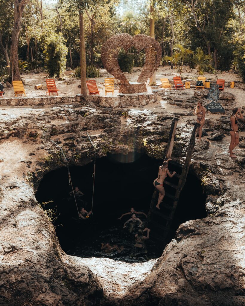 a deep sinkhole cenote showing many people jumping in and climbing out of casa cenoe in mexico