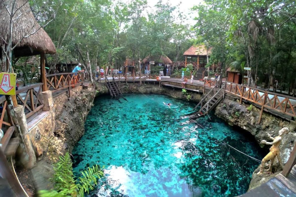 small sinkhole cenote with turqoise blue waters, surrounded by wooden walkway 