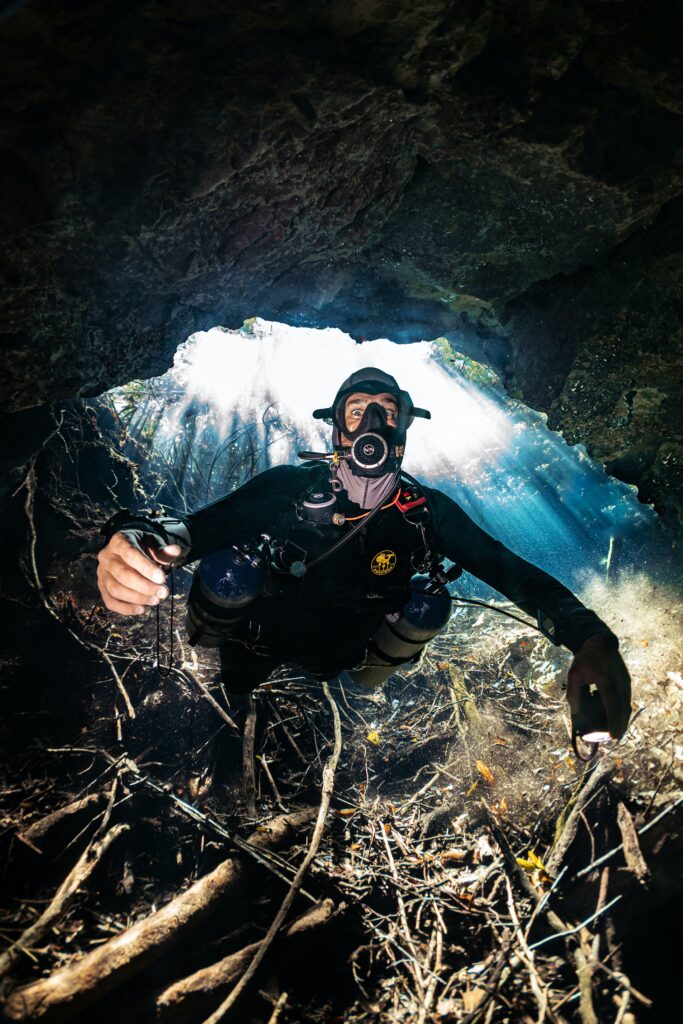 diver swimming through an underground cenote discovering the cave as light is pealing in from a hole 