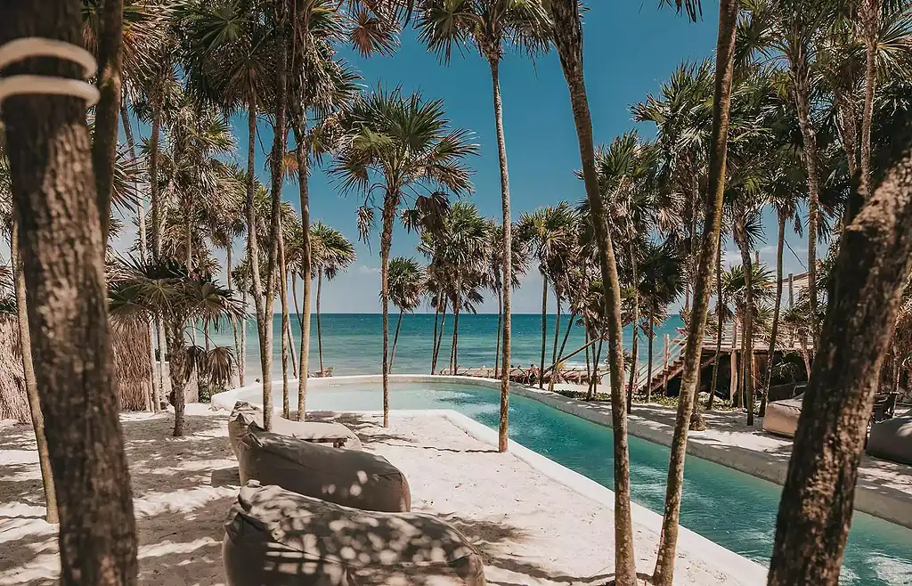 long pool with large sofas and several palm trees and a view of the Caribbean sea at Papaya playa project tulum