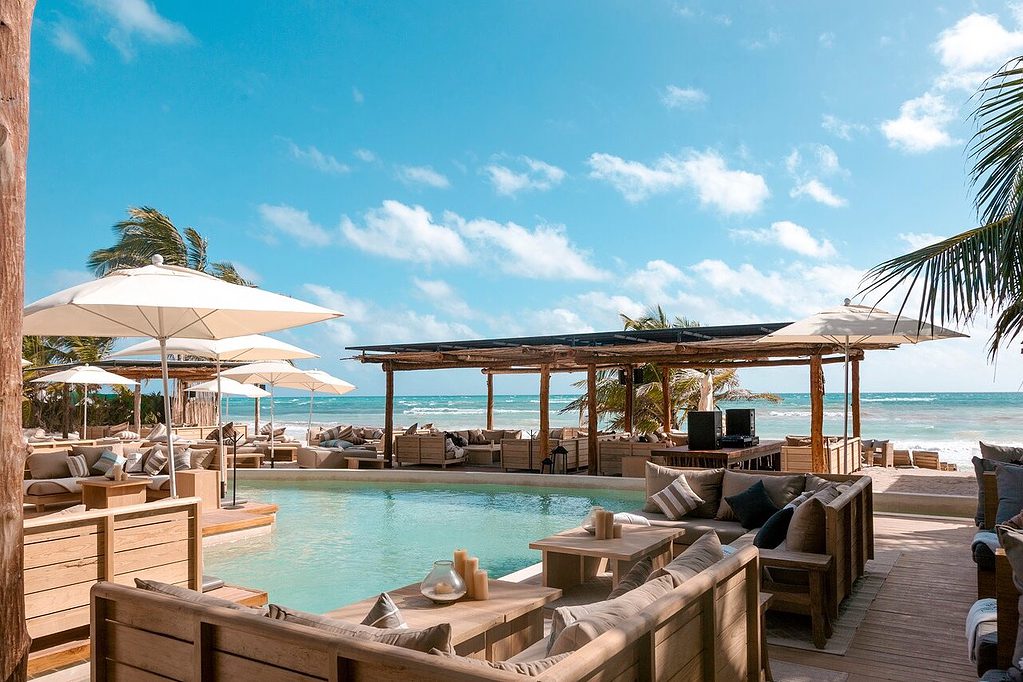 beachclub area at rosanegra featuring a pool, lounge chairs, sofas, palm trees and the sea