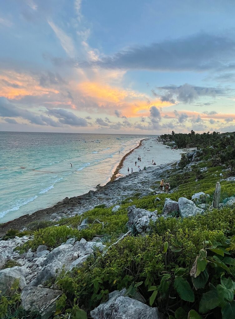 view from hill showing the entire tulum main beach shoreline, featuring rich greenery and sunset amongst the clouds