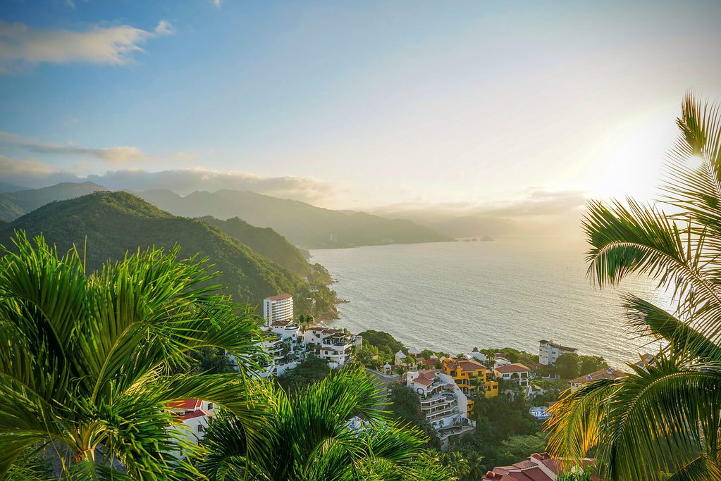 sunset coming in among dense forests on the mountains and beach shoreline full with condos in Puerto Vallarta, Mexico