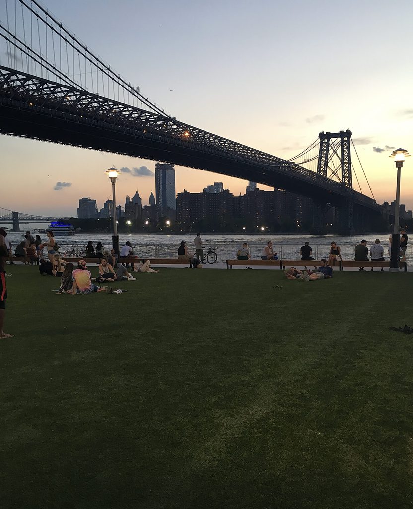 several locals are sitting on the grass during sunset at Domino Park in Williamsburg, Brooklyn 