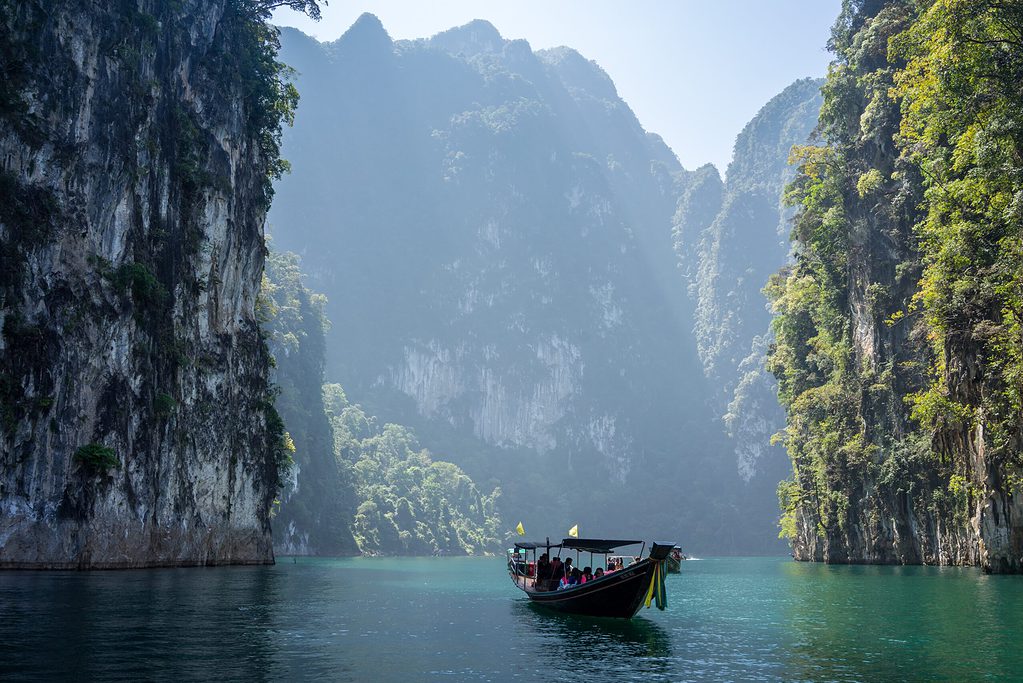 views of the river alongside tall high green mountains from the view of a boat in Khao Sok National Park in Thailand