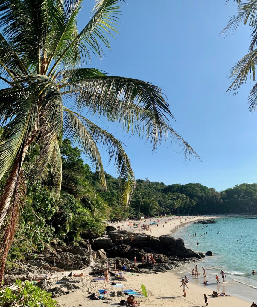 several tourists crowded on Banana Beach, a secluded tranquil beach in Phuket with turquoise waters and several palm trees