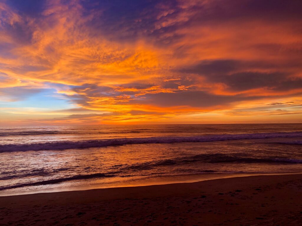 Vibrant orange and multi-colored sunset casting reflections over the shoreline at Bang Tao Beach in Phuket, Thailand
