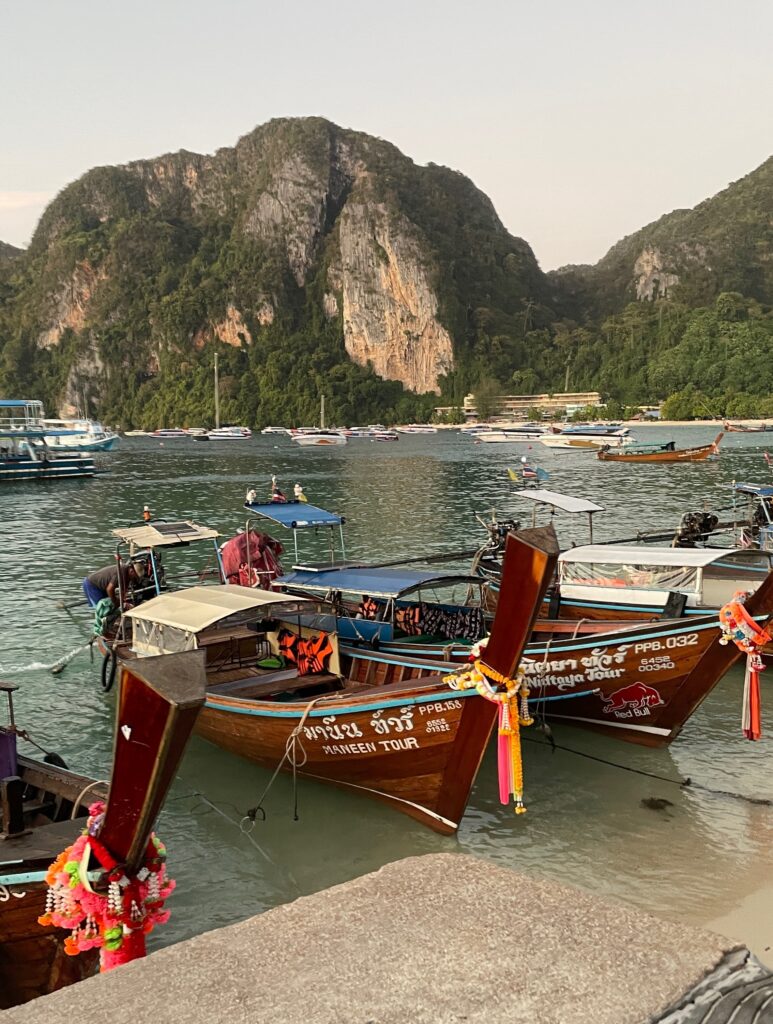 several Thai style longtail boats docked at the main pier in Phi Phi Don and a stunning backdrop of mountains and sea / is Phi Phi Island worth visiting / Koh Phi Phi Itinerary for 2 or 3 days