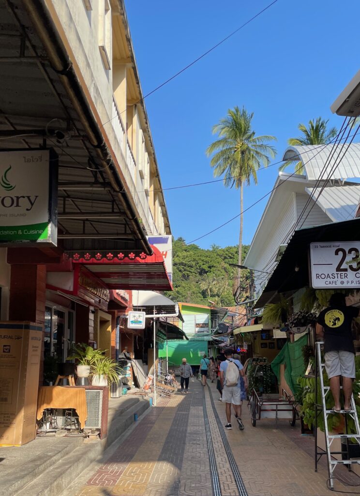 a street in Koh Phi Phi don with several shops on the side and tourist walking