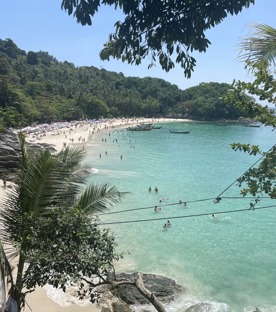 a crowded beach full of tourists surrounded by dense forests named Freedom Beach in Phuket, Thailand 