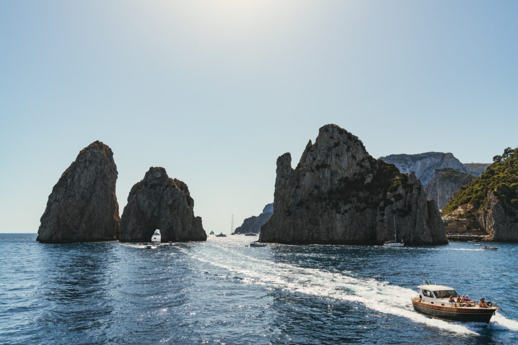 a yacht sailing along the coast of Capri, Italy with the famous arch rock in the background 