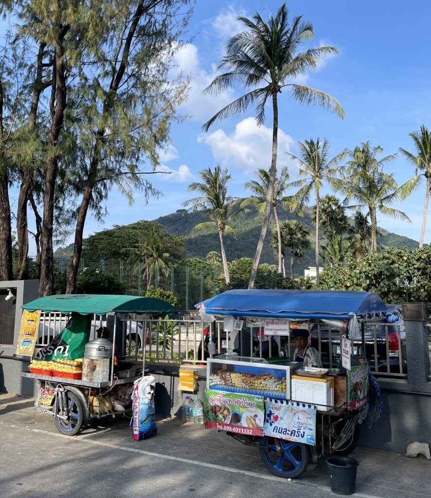 street food vendors at Kata Beach, with a beautiful mountainous range full of palm trees in the background in Phuket, Thailand