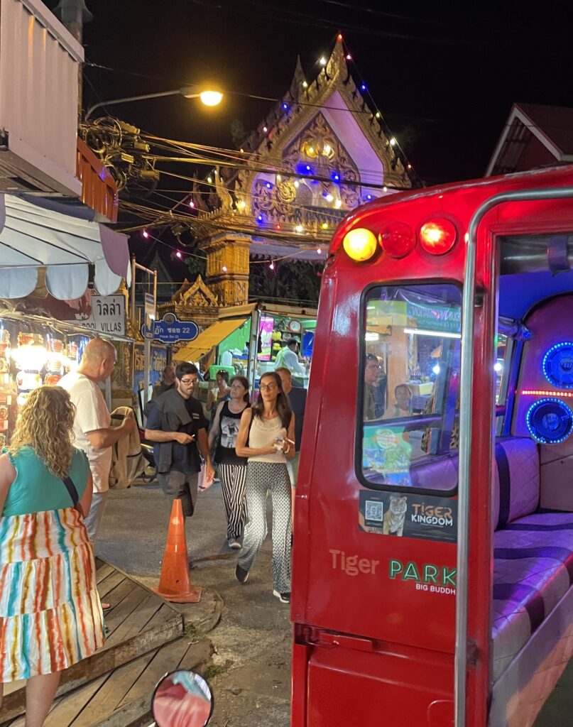 several tourists walking out and into the Karon Night Market in Karon Beach, Phuket, Thailand, tuk tuk scam is one of the popular scams in Phuket to watch out for