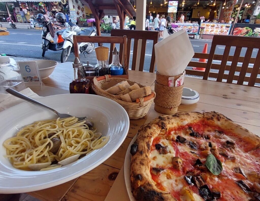 pizza and pasta being served at table with a street view at Napoli in Vespa restaurant in Karon Village Phuket