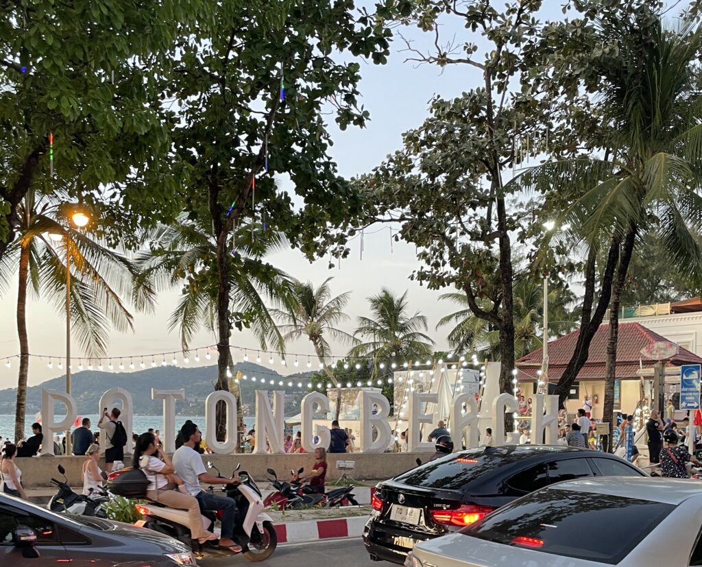 alternative white Patong Beach sign standing in front of Patong beach at sunset, surrounded by palm trees in Patong, Phuket / how to get from Phuket airport to Patong beach