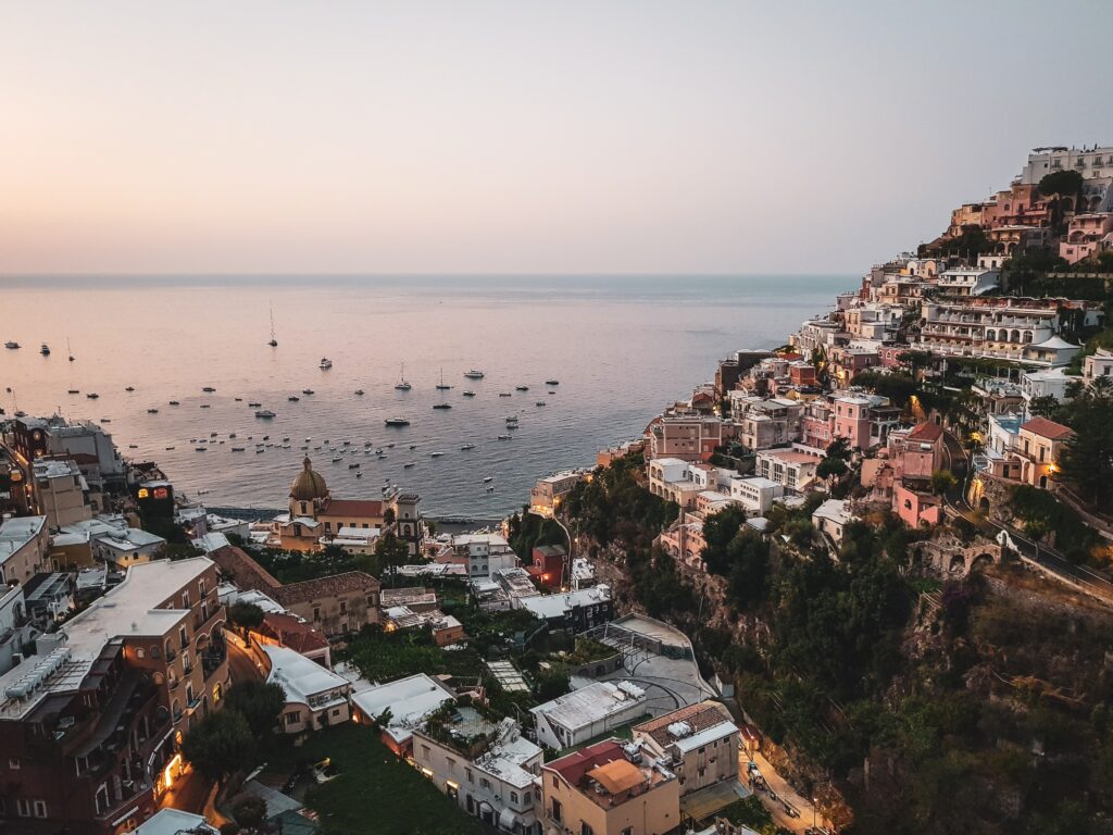 views of the hills of Positano with several boats anchored at the shores during sunset in Positano, Italy