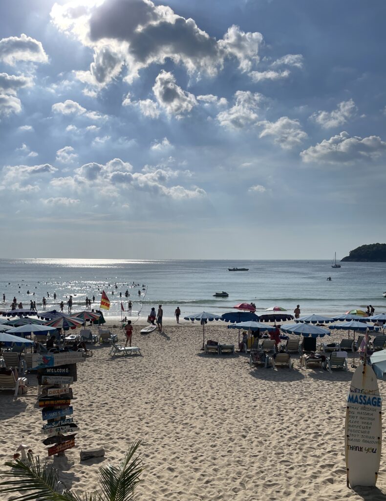 the sun pealing through clouds with several beachgoers in Kata Beach, Phuket