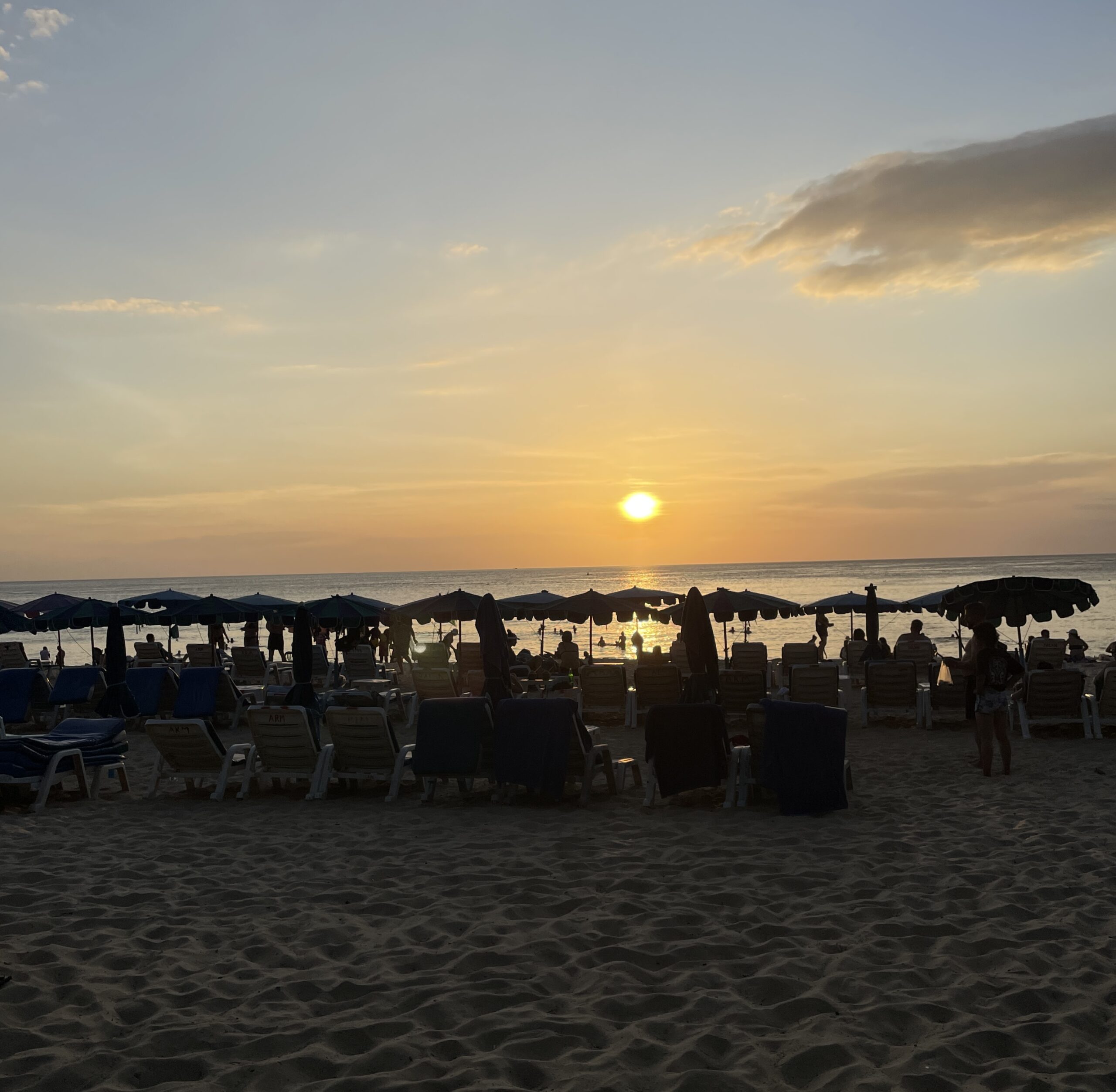 several beach lounge chairs, umbrellas with the sunset at Karon Beach in Phuket, Thailand