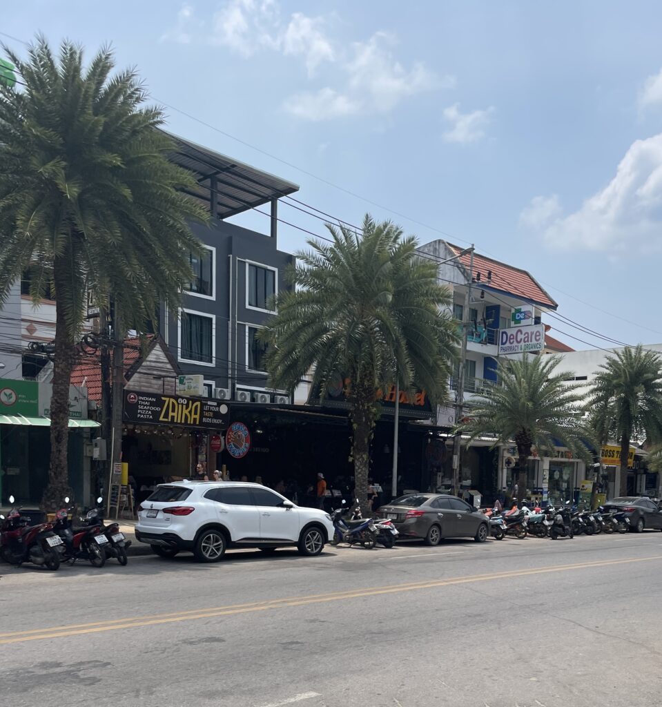 cars parked amongst palm trees on a main street in Ao Nang, Thailand