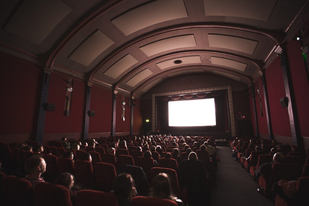 several movie goers in a cinema watching a movie on a bright screen 