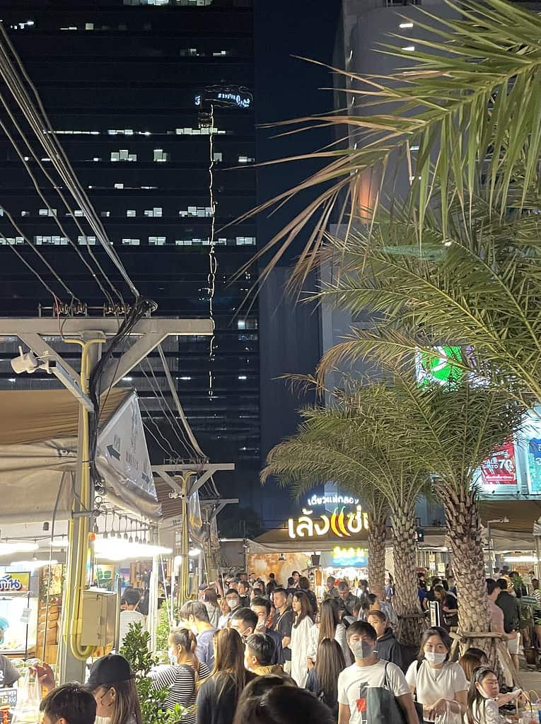 several locals and tourists walking amongst the many food stalls at Jodd Fairs, a popular night market in Bangkok, Thailand