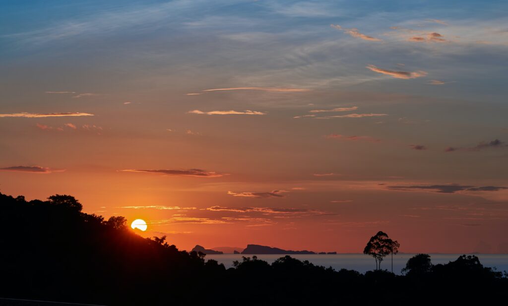 Vibrant orange sunset over the ocean in Koh Samui, Thailand, with silhouetted palm trees and a glowing horizon
