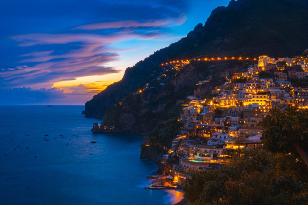 stunning vibrant sunset views of the hills full of hotels, villas and restaurants at night in Positano, Italy 
