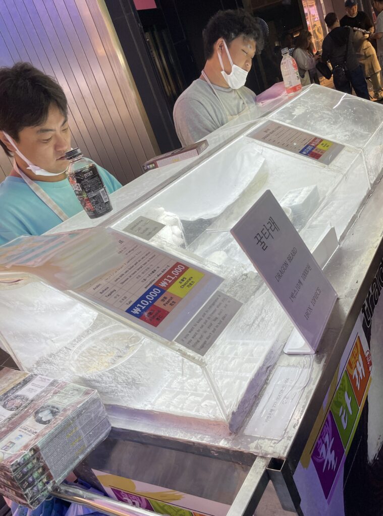 vendors making Korean taffy in an enclosed box from their stall at the night market in Myeongdong 