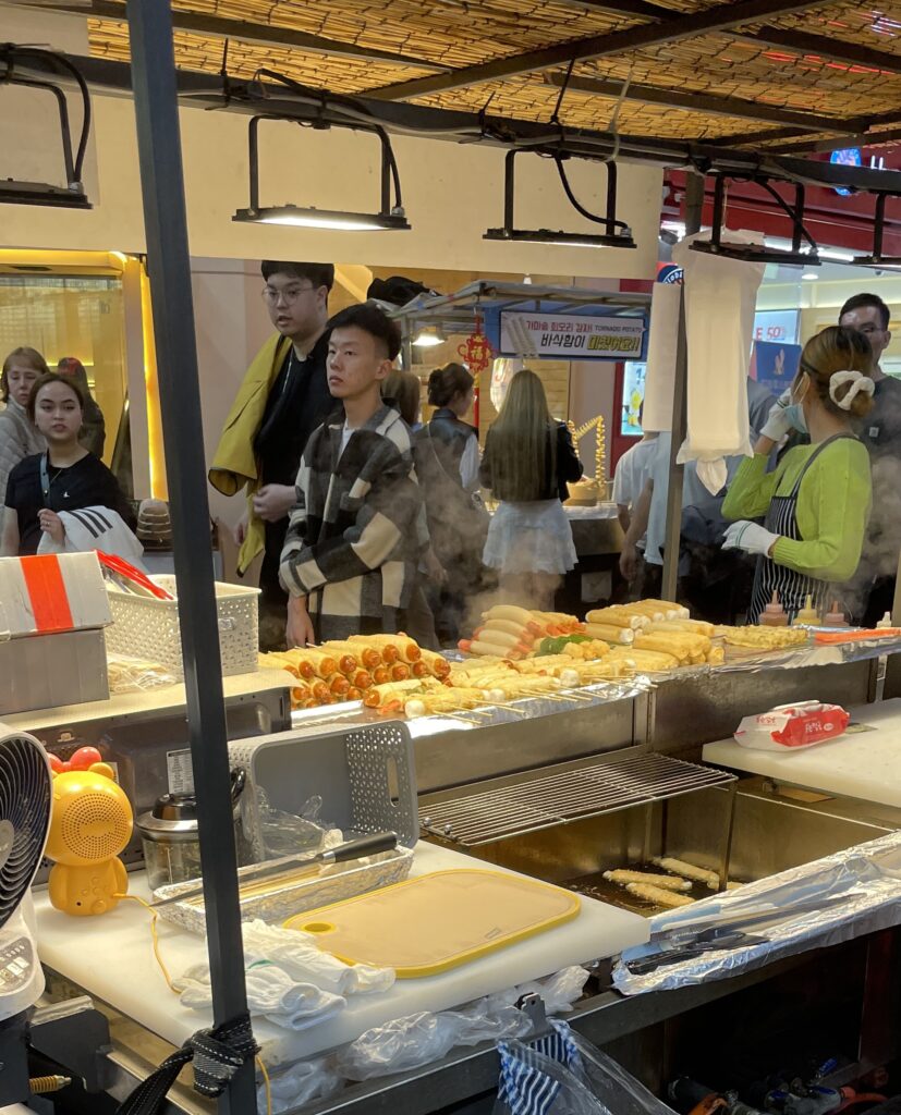 several Korean styled hot dogs being sold by a vendor at night market in Seoul
