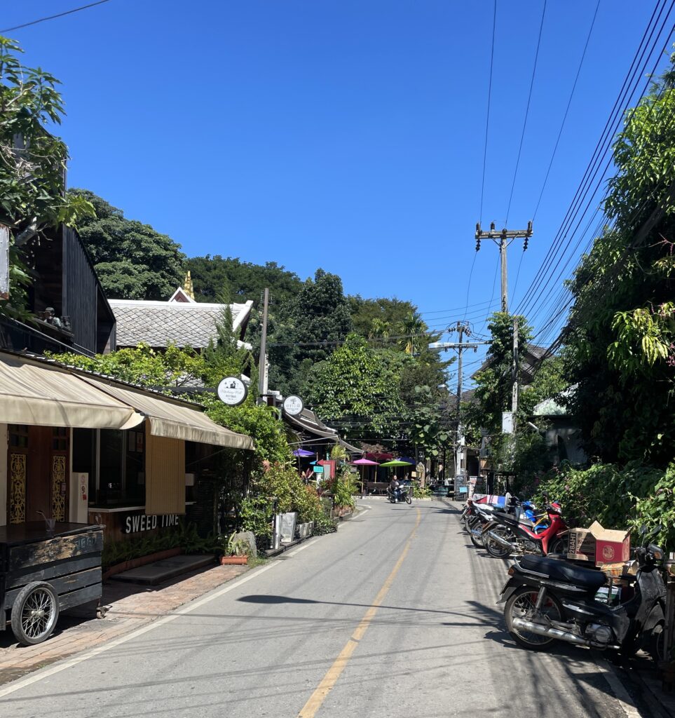 picturesque street in Pai with scooters parked on the side of the road, greenery ahead on a clear sky day 