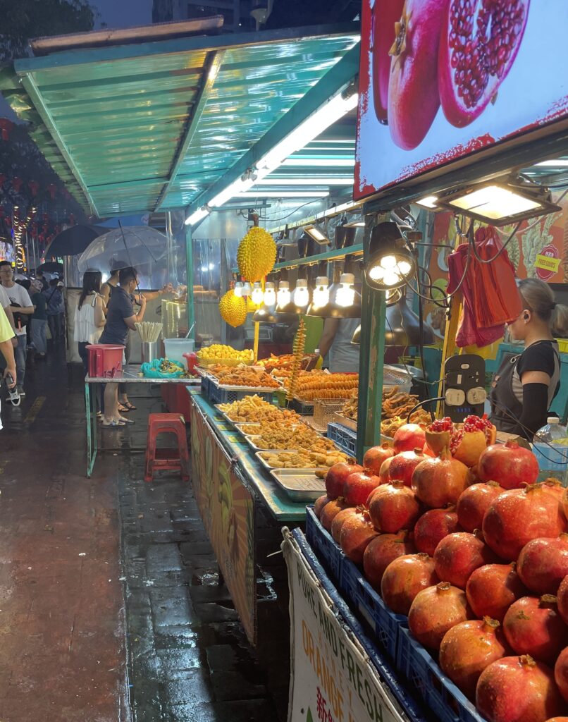 two street food vendors selling food at the Jalan Night Market, one has several fried foods and the other is selling fresh fruit