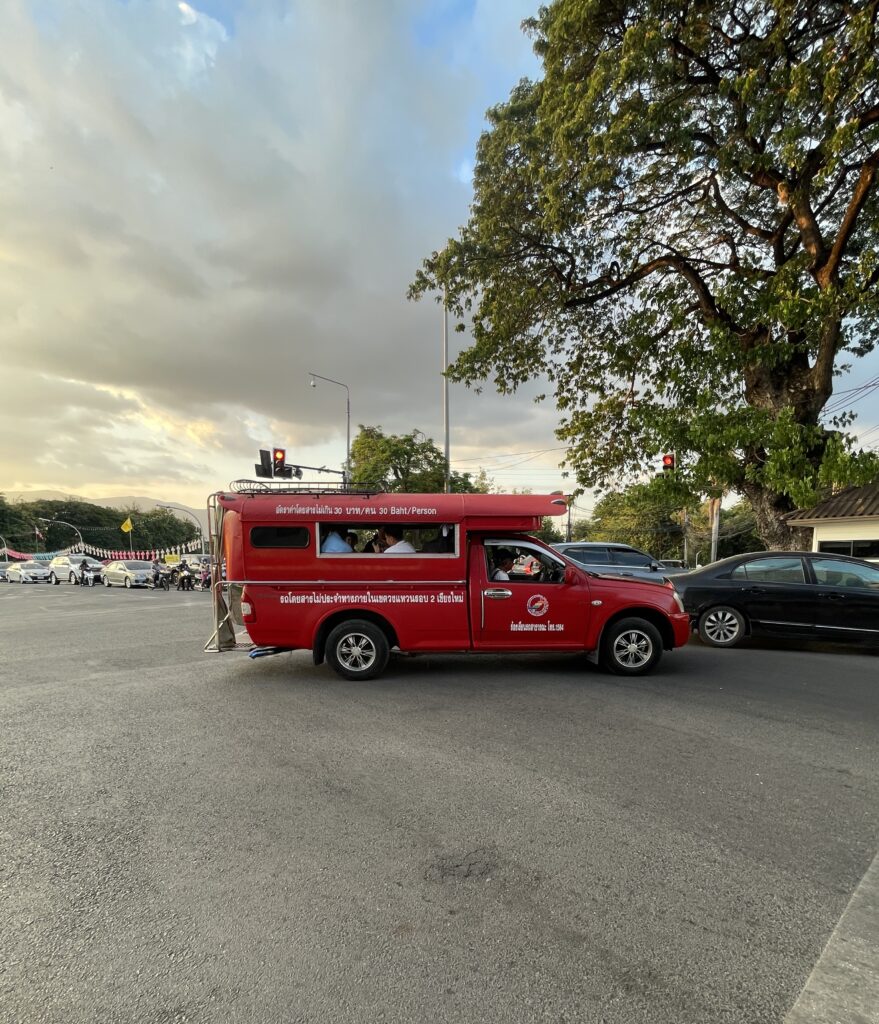 bright red songthaew shared taxi driving around Chiang Mai on a sunny day