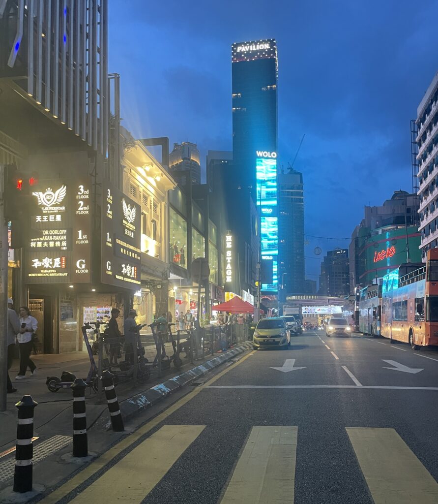 a known street in Kuala Lumpur at night with plenty of lights and advertisement signs in the distance 