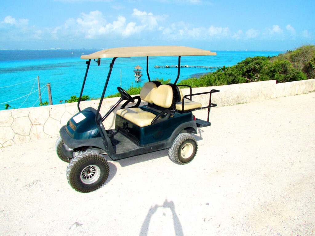 a golf cart parked street side with vibrant stunning turquoise blue waters in the distance in Isla Mujeres, Mexico