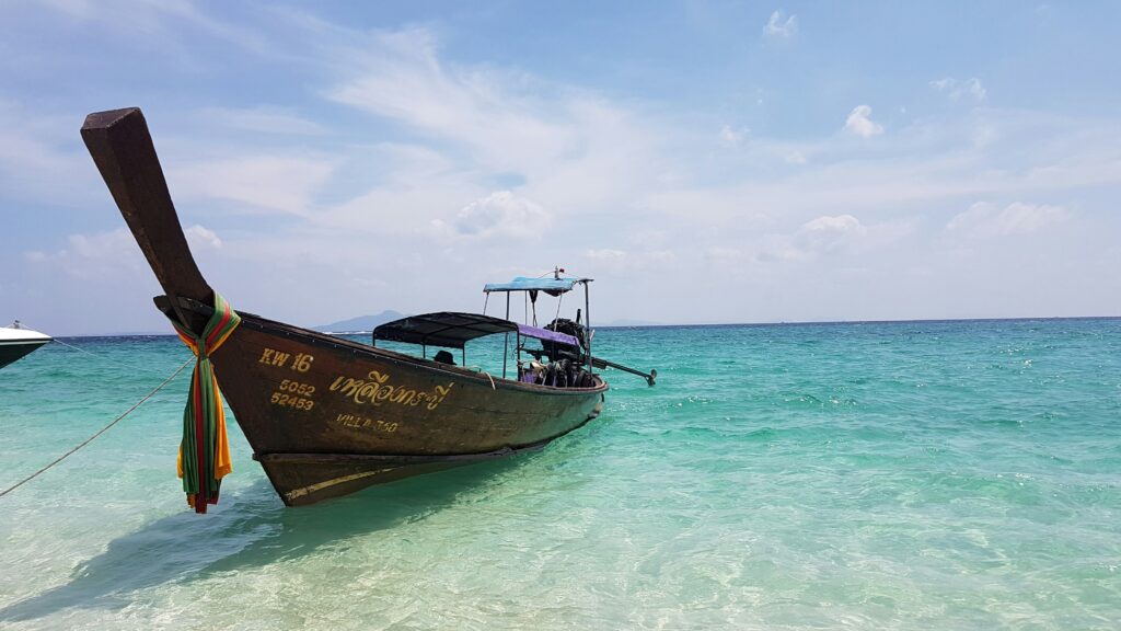 a Thai long tail boat anchored by the beach amongst crystal clear blue waters in Khlong Muang, Krabi