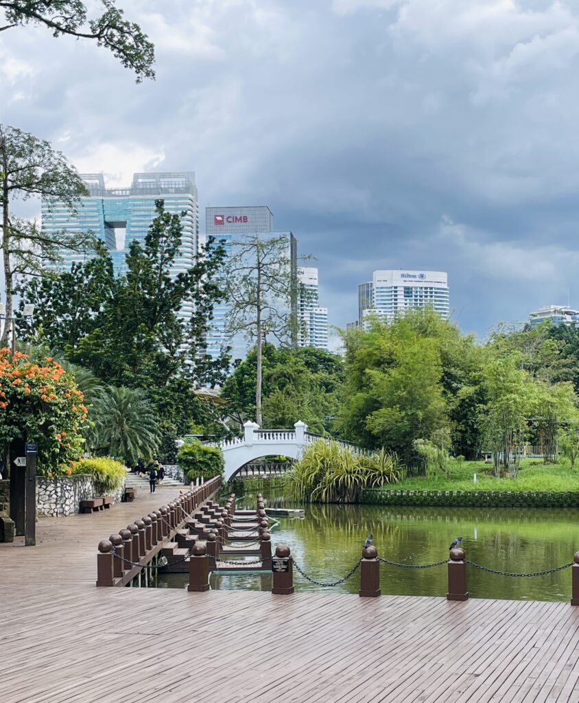 a charming white bridge over a small lake shown in the distance amongst plenty of greenery at the Perdana Botanical Gardens in Kuala Lumpur 