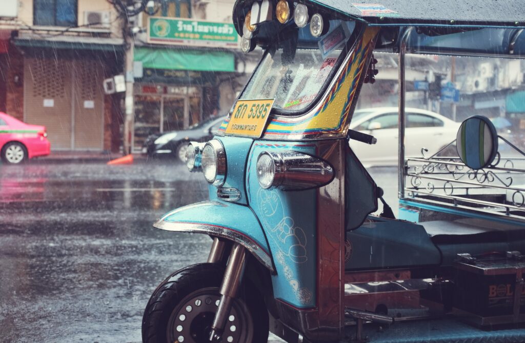 a tuktuk parked on the side of the road in Bangkok as rain is pouring down