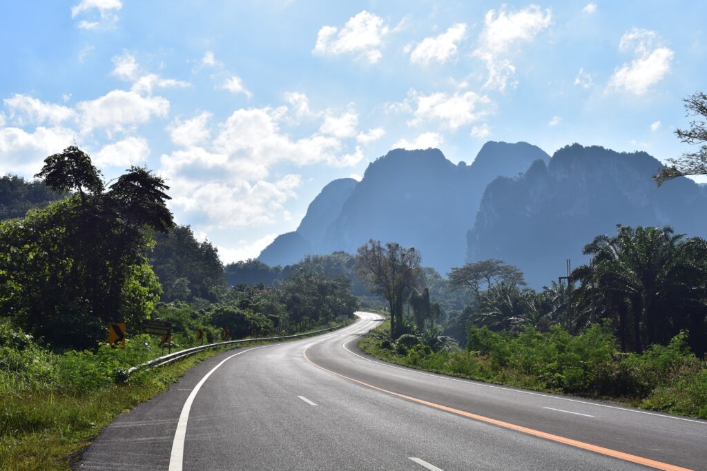 an empty winding road with plenty of greenery in the distance and large limestones on a clear sunny day in Thailand 