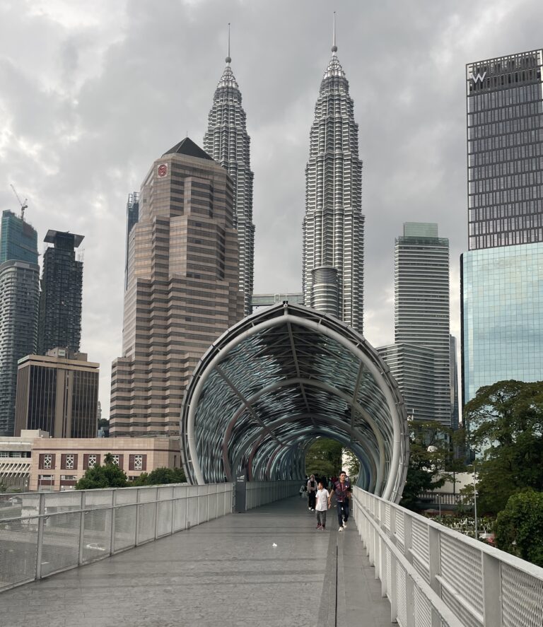 locals crossing the popular Solama link bridge in Kuala Lumpur with the cities skyline in the background featuring the famous Petronas Towers in Kuala Lumpur / latest scams in Kuala Lumpur