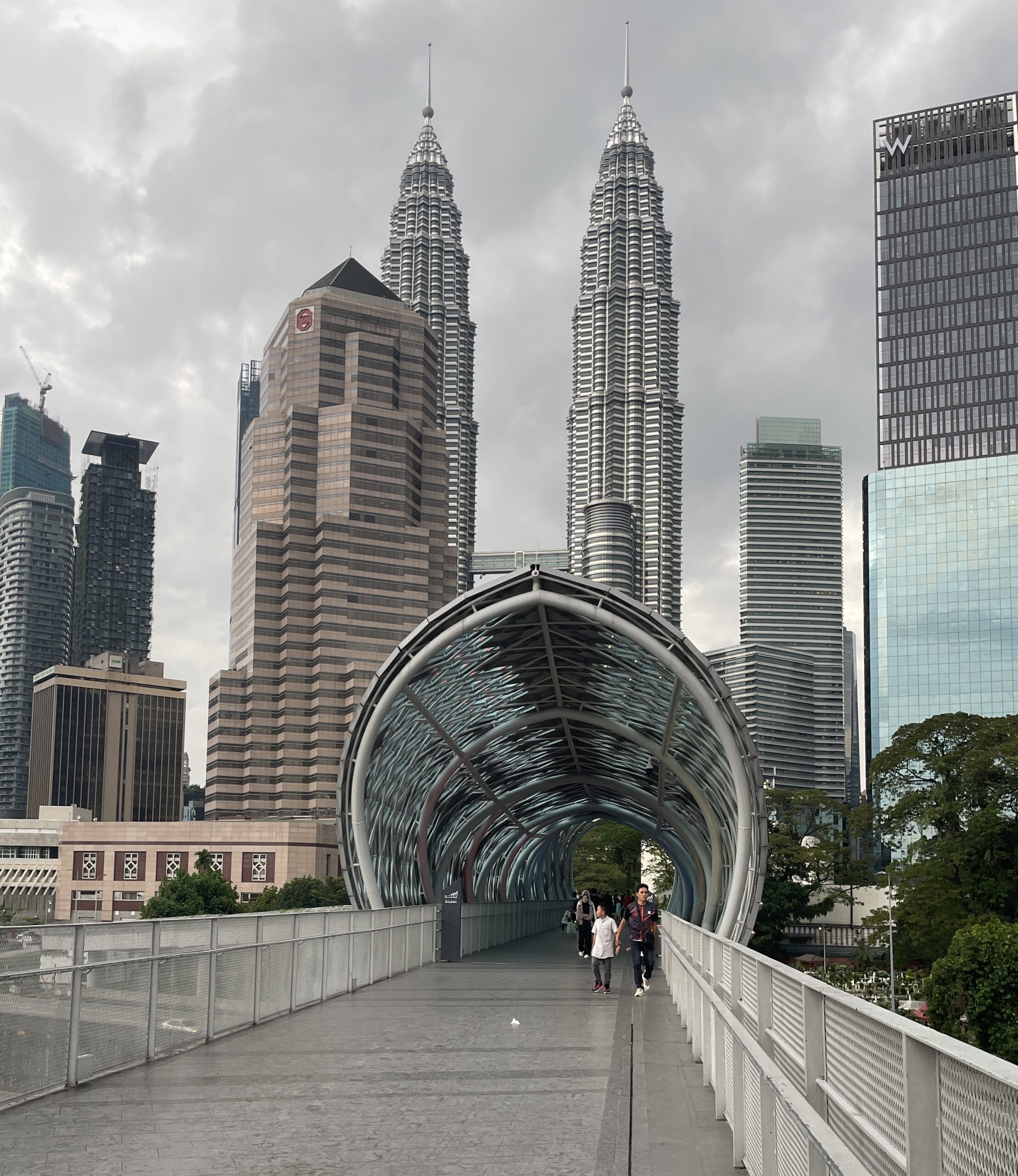 locals crossing the popular Solama link bridge in Kuala Lumpur with the cities skyline in the background featuring the famous Petronas Towers in Kuala Lumpur / latest scams in Kuala Lumpur