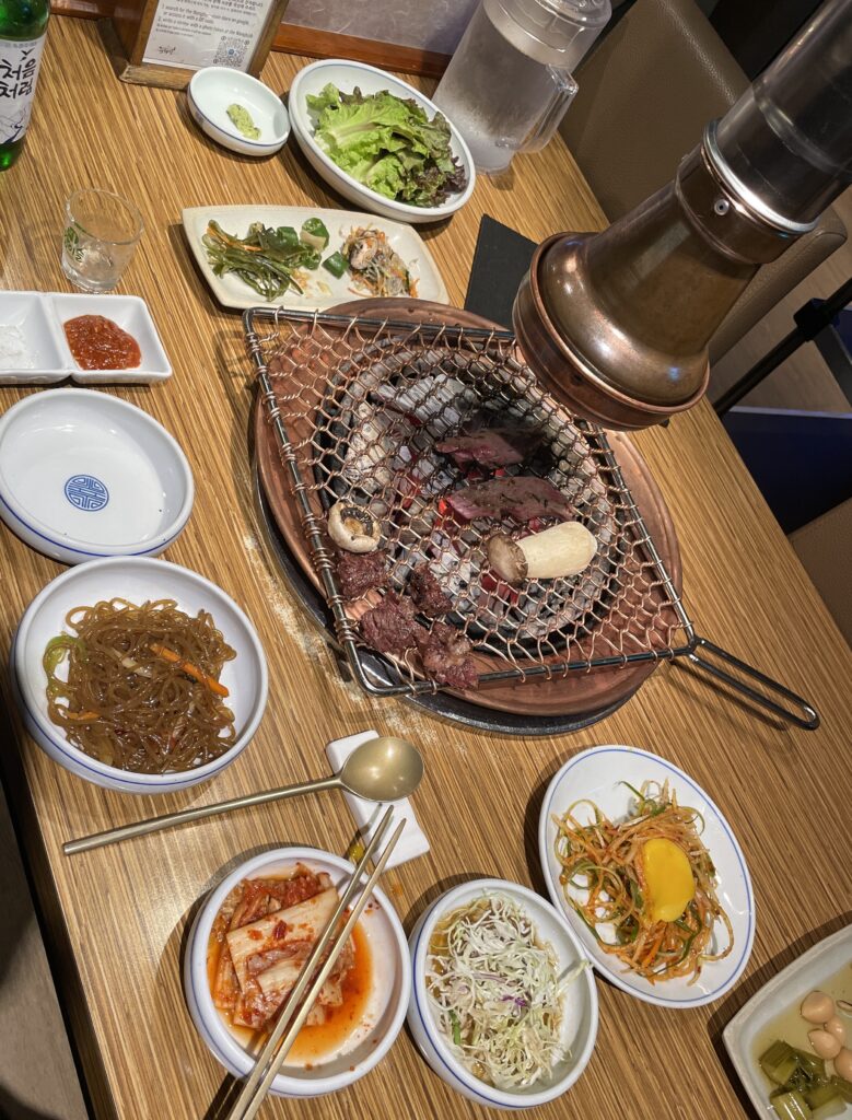 several beef cuts being cooked under hot charcoal surrounded by types of side dishes at Korean BBQ restaurant in Seoul 