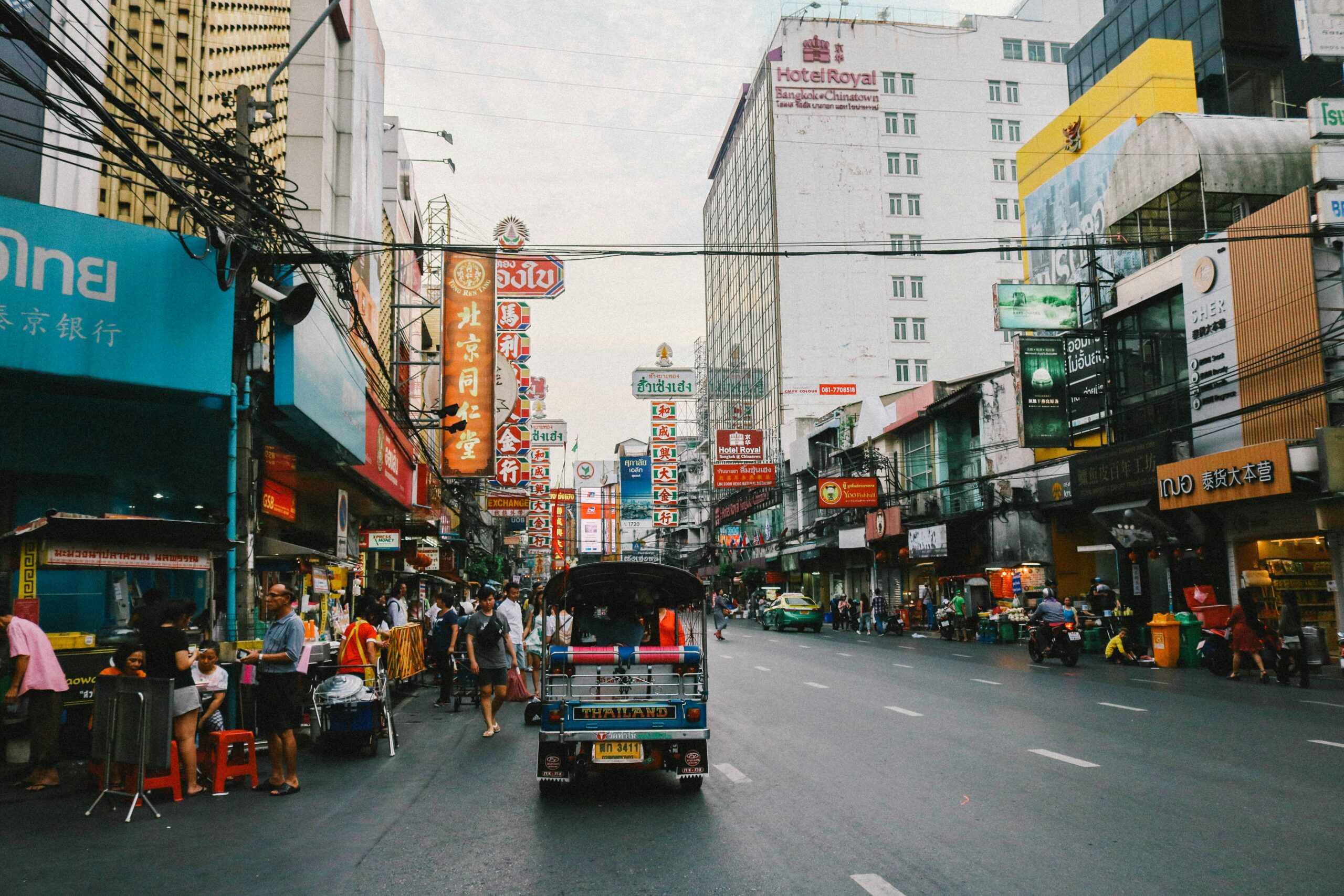 many locals and tourist dining on the busy streets of Bangkok as a Tuk Tuk is driving by / where to stay in Bangkok first time