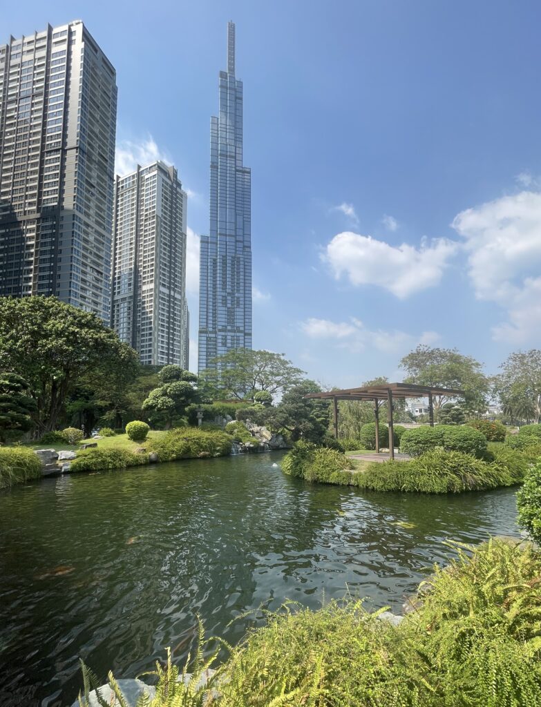 a pond full of koi fish at the Central Park amongst several skyscrapers in Ho Chi Minh City on a clear sky sunny day
