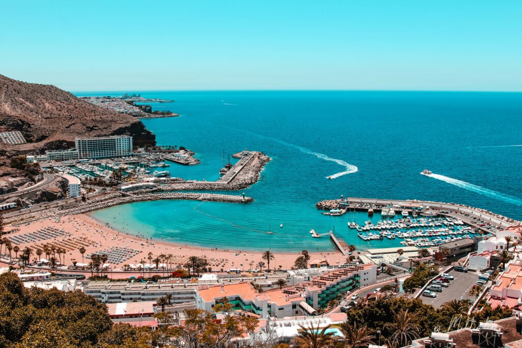 many beach goers sunbathing and plenty of boats docked at a marina in Gran Canaria, Spain 