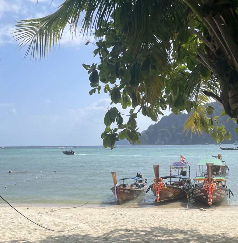 three longtail boats docked by the beach shoreline on a sunny day in Koh Phi Phi, Thailand