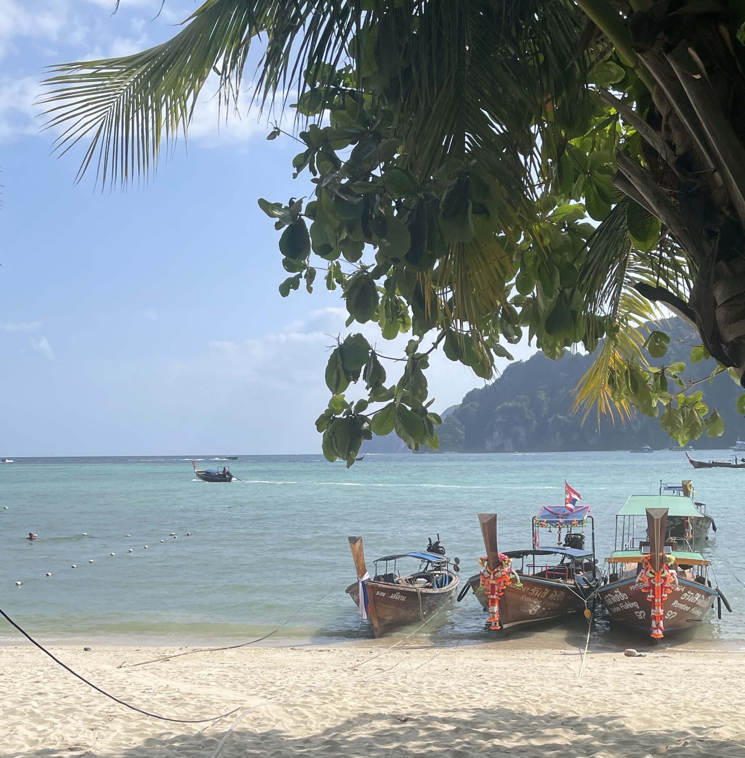 three longtail boats docked by the beach shoreline on a sunny day in Koh Phi Phi, Thailand
