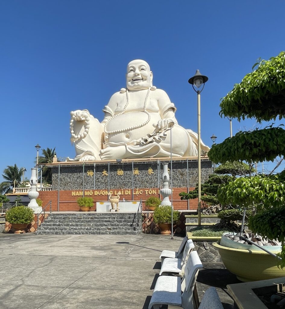 the famous large laughing buddha statue standing tall on a sunny day at the Vinh Trang Pagoda temple in Vietnam